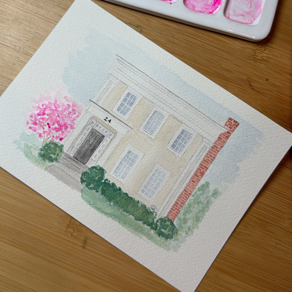 Watercolor painting of a house on paper with a watercolor palette in the background.