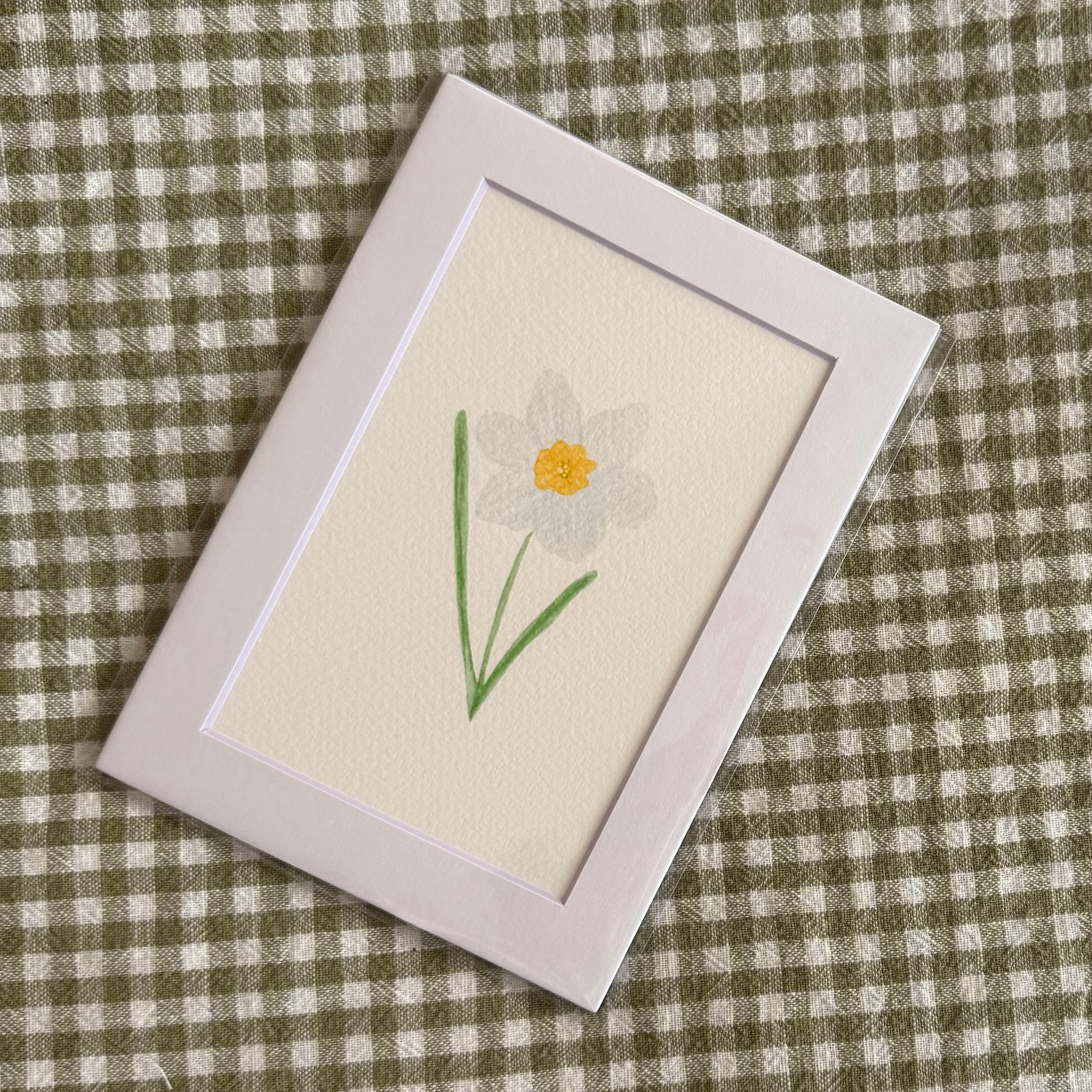 Small embroidered card with a narcissus flower design on a green checkered fabric background