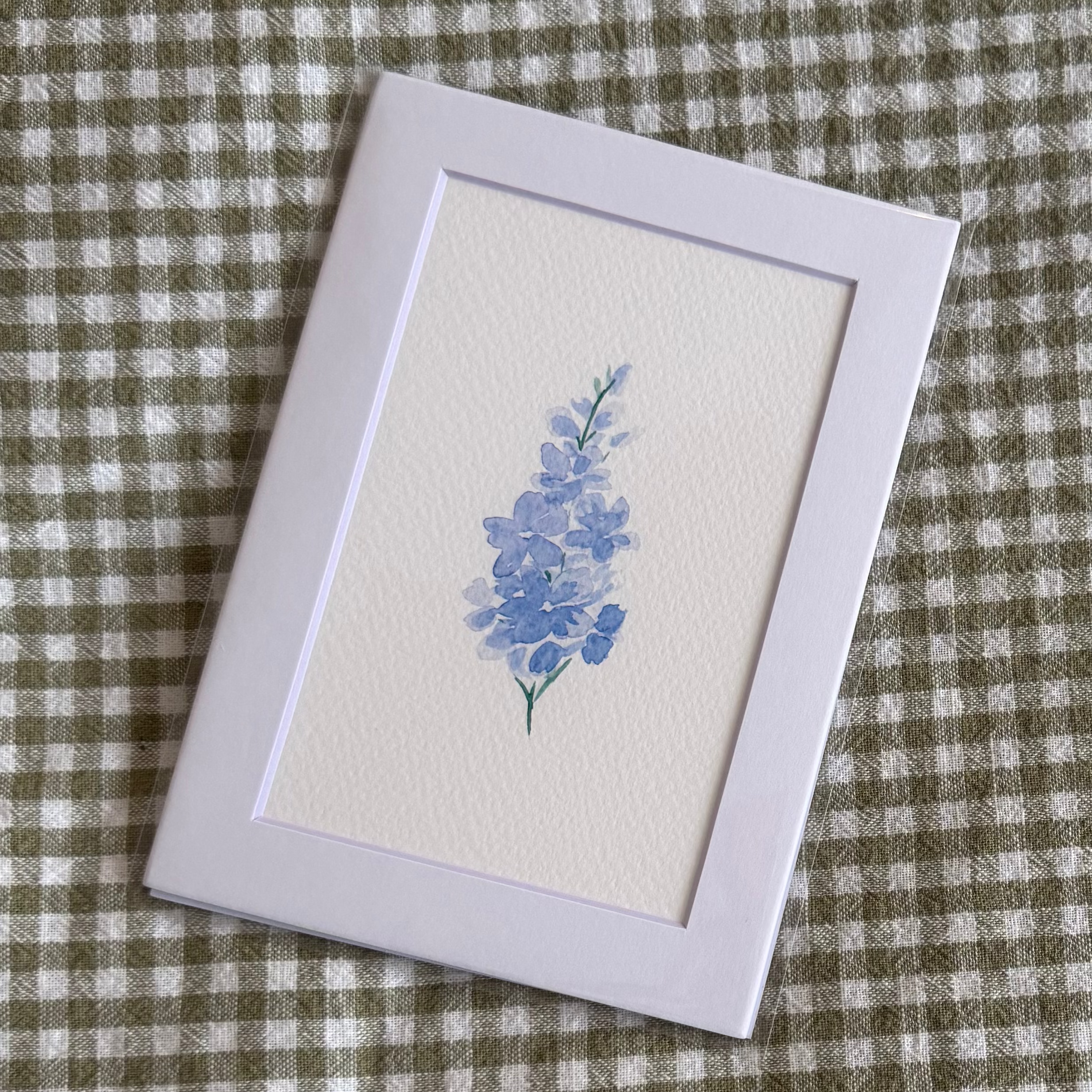 Small white mat with a larkspur painting on a green and white checkered background